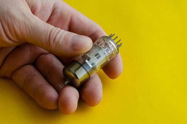 Male hand holds a vacuum tube on a yellow background. A radio tube that came out of the operation in a male hand. Collecting radio parts or recycling. Selective focus. - Φωτογραφία, εικόνα