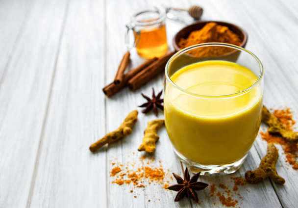 Yellow turmeric latte drink. Golden milk with cinnamon, turmeric, ginger  and honey over white marble background. - Photo, Image