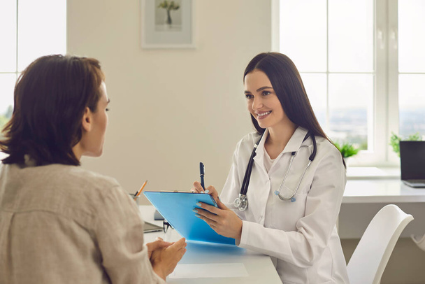 Young smiling female doctor discusses the diagnosis with a patient in a medical office. - 写真・画像