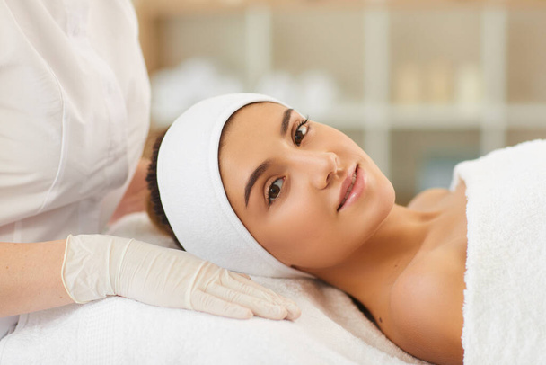 Beautiful young woman looking at camera while lying on salon table after skin care procedures - Фото, изображение