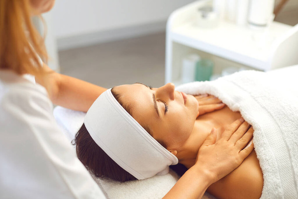 Woman patient getting manual relaxing rejuvenating massage for face and shoulders from therapist - Photo, Image