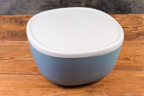 Plastic blue-gray salad bowl with closed gray lid on the rustic table - Valokuva, kuva