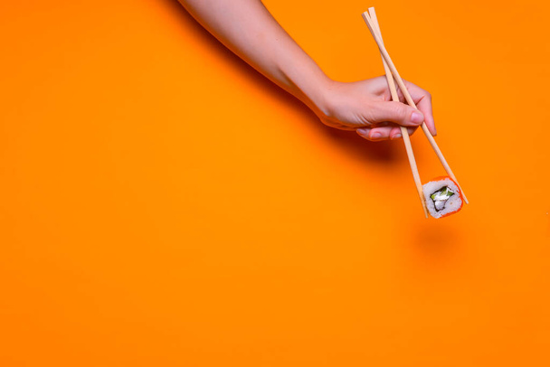 Vibrant sushi set, creative idea concept. Holding Sushi in chopsticks, in hand. Traditional Japanese cuisine concept. Sprinkled with sesame seeds. Over bright color background. Copy space banner. - Zdjęcie, obraz