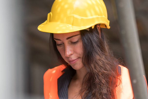 Προσωπογραφία μιας απορροφώμενης εργάτριας εργοστασίου που φοράει κράνος και γιλέκο ασφαλείας - Φωτογραφία, εικόνα