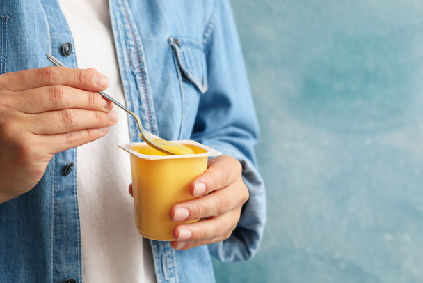 Woman hold plastic cup of sour cream yogurt and spoon against blue background - Fotografie, Obrázek