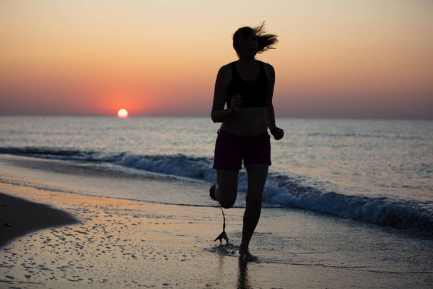 海での日の出を背景にした女性アスリートのシルエット - 写真・画像
