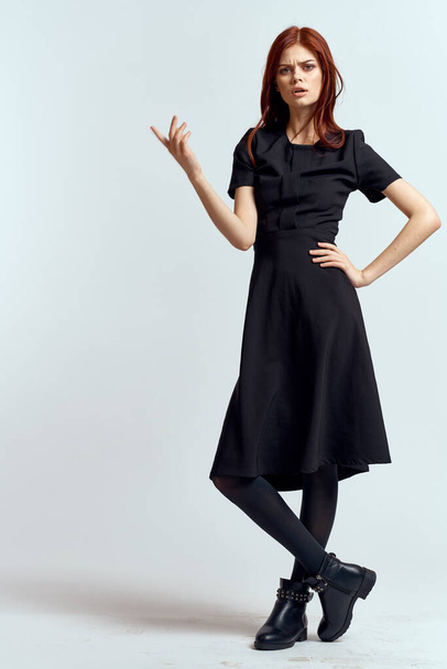 A woman in a black dress on a light background and pantyhose shoes red hair and pose in full growth - Fotoğraf, Görsel
