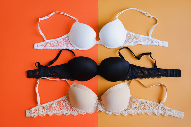 Bra of white, black and beige color on orange and yellow background, overhead view. Women's lingerie collection - Photo, Image