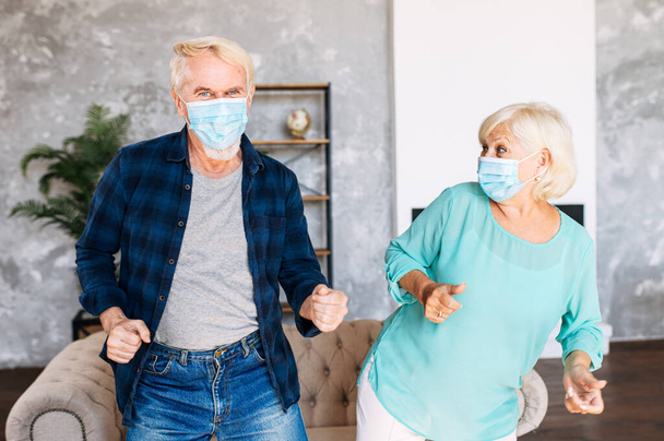 Senior couple wearing face masks dancing indoors - Foto, afbeelding