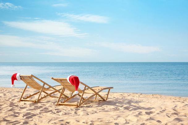 Sun loungers with Santa's hats on beach, space for text. Christmas vacation - Foto, imagen