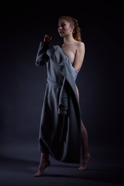 Slender naked girl in a coat poses in front of the camera - Foto, afbeelding