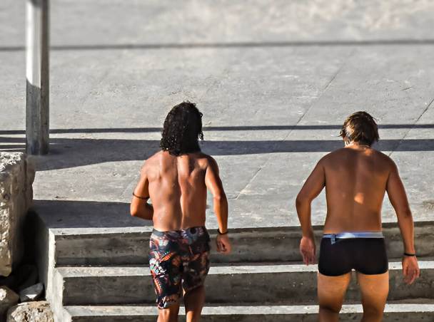 Δύο άνδρες με μαγιό τρέχουν σε ένα πεζοδρόμιο με σκάλες κοντά στην παραλία - Φωτογραφία, εικόνα