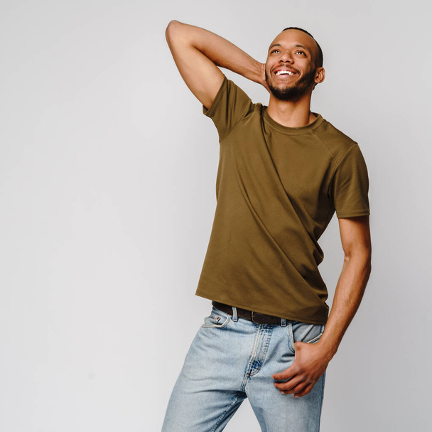 Joyful friendly african-american young man in green t-shirt over light grey background with copy space - Foto, Imagem