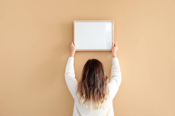 Mujer colgando marco de foto en blanco en la pared - Foto, Imagen