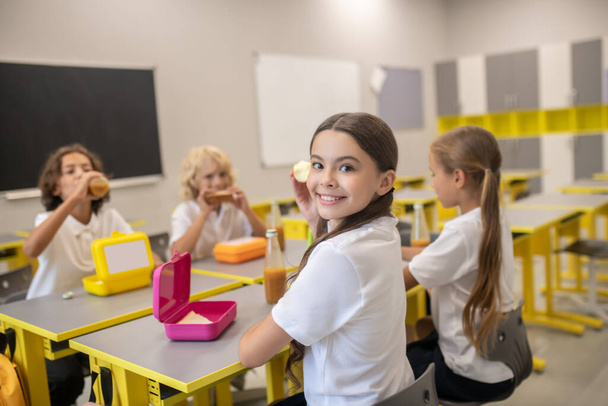 Schoolchildren having lunch in the classrom and looking happy - Фото, изображение