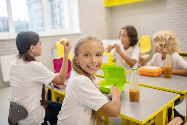Schoolchildren having lunch in the classrom and looking excited - Foto, imagen