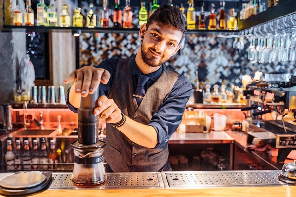 Alternative method of brewing coffee. Attractive young barista making coffee using an press. Gently presses on flask, passing the coffee liquid through the filter. Coffee without milk and sugar. - Photo, Image