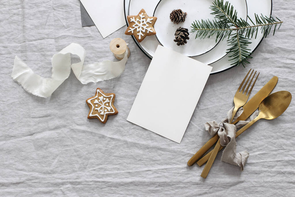 Plates, pine cones on table cloth. Winter festive greeting cards mockup scene. Golden cutlery,gingerbread cookies and fir tree branches. Christmas table setting. Holiday background. Flat lay, top view - Φωτογραφία, εικόνα