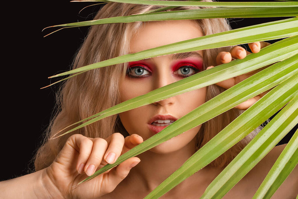 Young woman with beautiful eyeshadows and tropical leaf on dark background - Фото, зображення