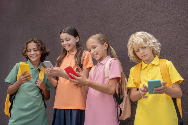 Four kids standing next to each other with smartphones in hands - Fotó, kép