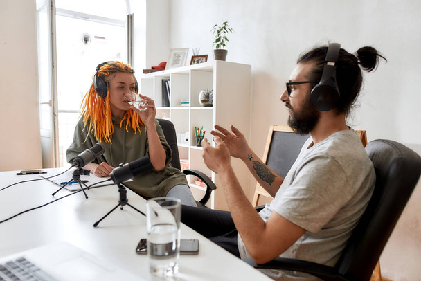 Two bloggers, young man and woman in headphones looking at each other while talking, recording conversation, interview for video blog - Fotó, kép