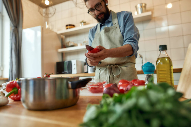 Young man cook holding, cutting tomatoes while preparing healthy meal with vegetables in the kitchen. Italian cuisine concept - Valokuva, kuva
