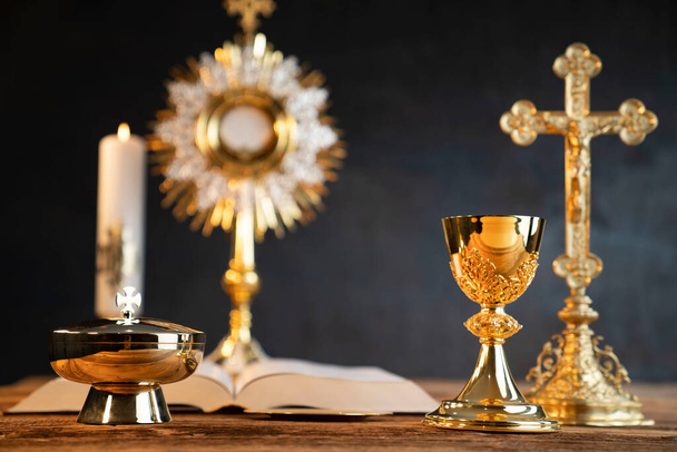 Catholic religion concept. Catholic symbols composition. The Cross, monstrance,  Holy Bible and golden chalice on wooden altar.  - Photo, Image