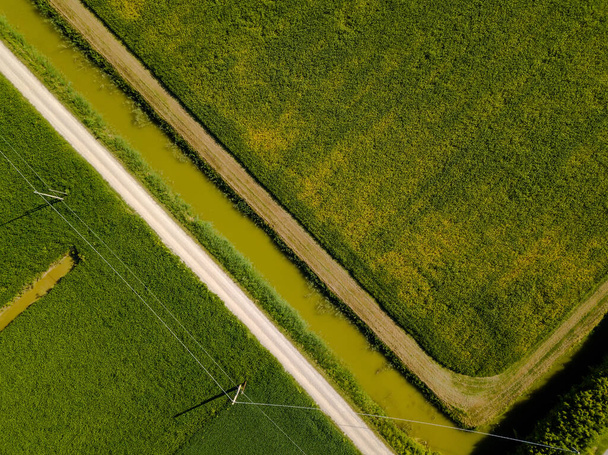 Image aérienne de champs agricoles avec des ruisseaux, des lignes électriques et des pistes de saleté de différentes couleurs en forme géométrique vue d'en haut à l'aide d'un drone - Photo, image