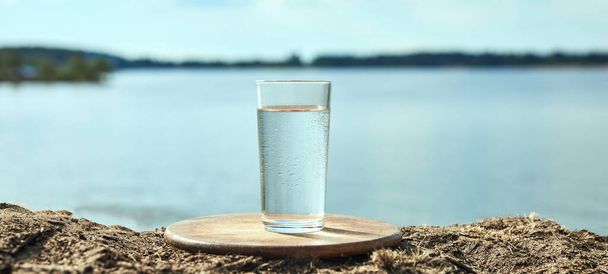 Clear fresh water in a glass against background of river or lake. Healthy food and environmentally friendly water. - Photo, image