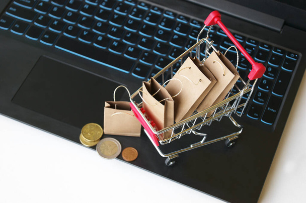 Mini shopping cart with small craft bags on the background of the keyboard. Online shopping concept. Convenience to shop without leaving home. - Photo, Image