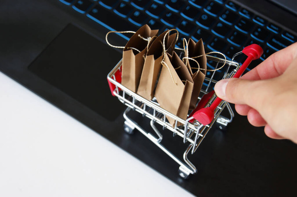 Mini shopping cart with small craft bags on the background of the keyboard. Online shopping concept. Convenience to shop without leaving home. - Photo, Image
