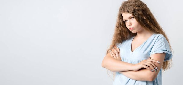 Offended pensive girl with curly long hair posing isolated on white background. People lifestyle concept. Holding hands crossed, looking at camera. Copy space for your text - Photo, Image