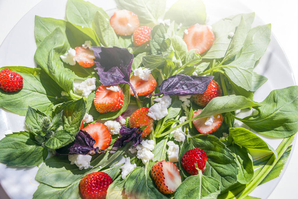 Ensalada de verduras de verano con fresas frescas, albahaca, mozzarella sobre fondo blanco en el jardín en el día soleado. El concepto de nutrición adecuada y alimentación saludable. Comida orgánica y vegetariana. De cerca. - Foto, imagen