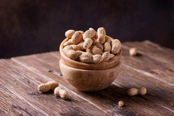 Roasted peanuts in wooden bowl on dark background selective focus image - Foto, afbeelding