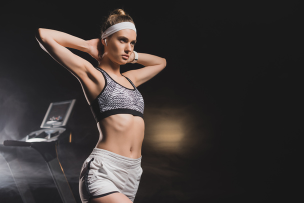 Sportswoman with hands behind head standing near treadmill in gym - Foto, imagen