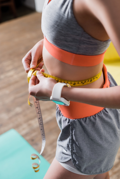 Cropped view of sportswoman measuring waist with tape at home - Photo, Image