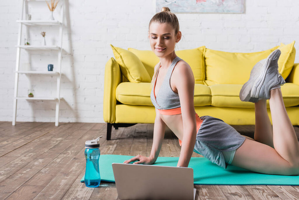 Sportnő gyakorló közelében laptop és üveg víz fitness mat otthon - Fotó, kép