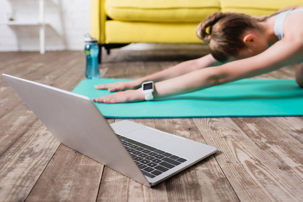 Close up view of laptop near sportswoman stretching on fitness mat at home - Photo, Image