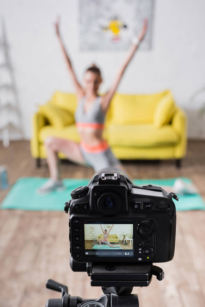 Selective focus of young sportswoman exercising near digital camera on tripod at home  - Foto, afbeelding
