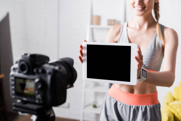 Vue recadrée d'une sportive joyeuse montrant une tablette numérique avec écran blanc à l'appareil photo numérique  - Photo, image