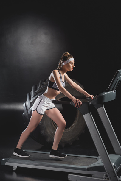 Sportswoman working out on treadmill near tire in gym  - Fotó, kép