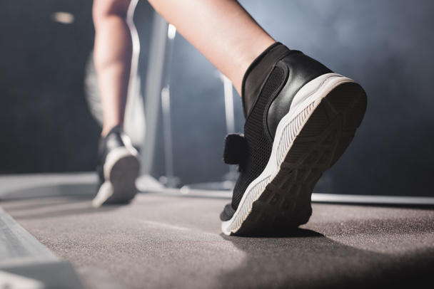 Selective focus of sportswoman in sneakers training on treadmill in gym  - Foto, Imagen