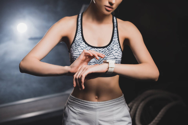 Cropped view of young sportswoman using smart watch in sports center with smoke  - Foto, Imagem