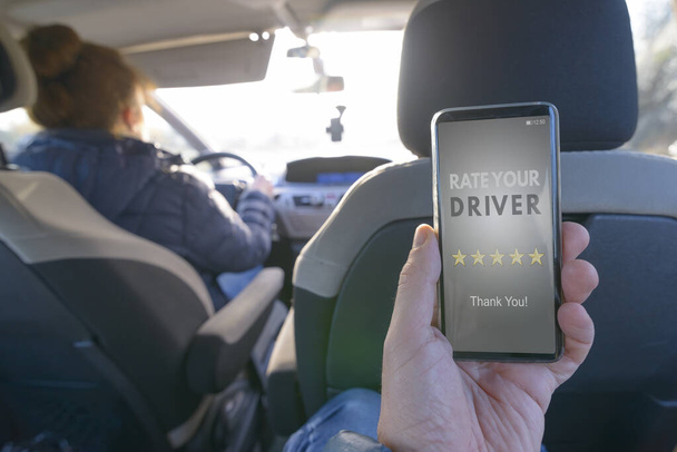 Yolcu arabanın arka koltuğunda oturuyor ve bir sürücüyü değerlendirmek için akıllı telefon uygulamasını kullanıyor. Taksi ya da akran paylaşım konsepti için modern akran - Fotoğraf, Görsel