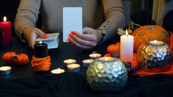 Sfocato indovino di mani che tengono carte bianche e carte di tarocchi sul tavolo vicino a candele accese a lume di candela. Concetto di previsione. . Foto di alta qualità - Foto, immagini