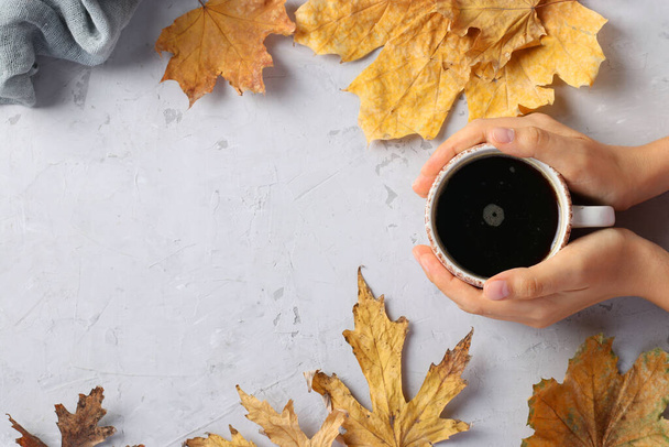 Keret őszi levelekkel és egy csésze kávé női kézben szürke háttér, felülnézet, hely a szöveg - Fotó, kép