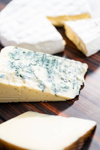 Variety of large gourmet cheese wedges on a dark wooden background. - Foto, Bild