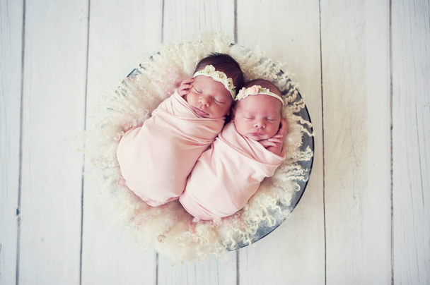 Newborn twins wrapped in a wrap sleeping on fluffy pad in bowl. Babies lie together. Sibling love from birth - sisters. - Photo, Image
