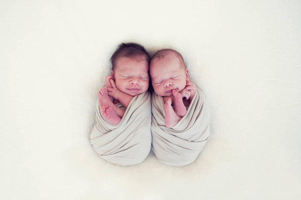 Gemelos recién nacidos envueltos en una envoltura durmiendo sobre una manta. Los bebés yacen juntos. Amor entre hermanos desde el nacimiento - hermanas, hermanos. - Foto, imagen