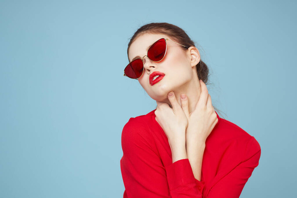 Koyu renk gözlüklü, kırmızı dudaklı, cazibeli stüdyo mavi arka planlı bir kadın. - Fotoğraf, Görsel